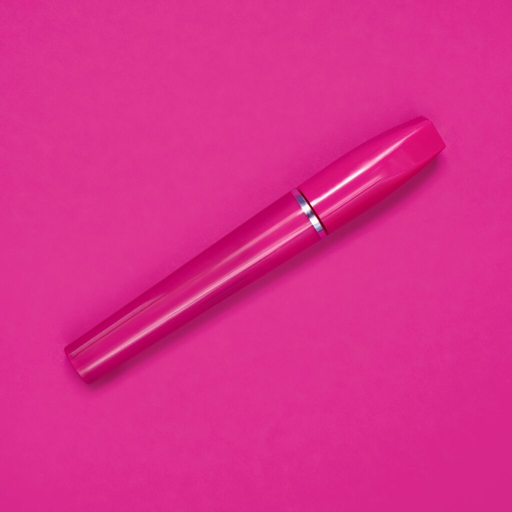 Close-up of a bright pink mascara tube against a matching pink background, emphasizing cosmetics.