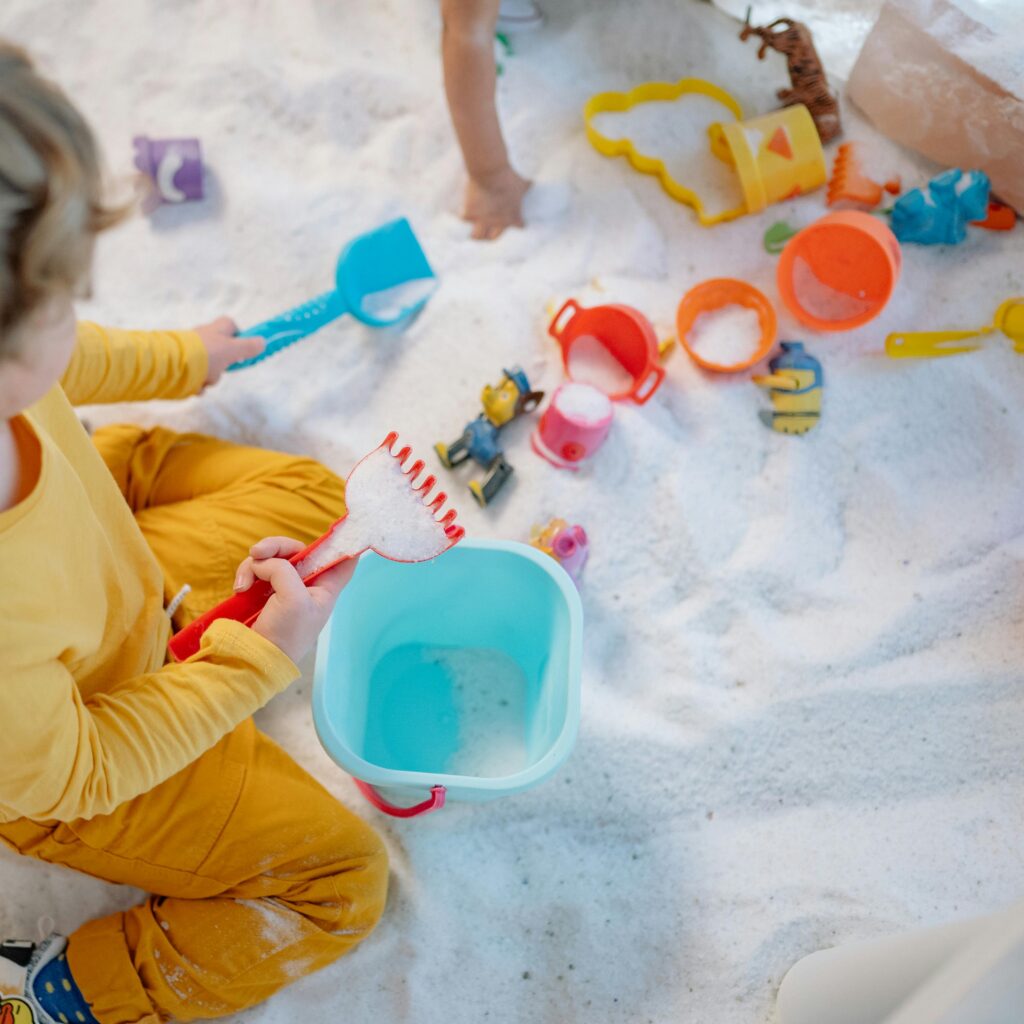 Top view of children playing with colorful toys in the sand, enjoying outdoor fun.